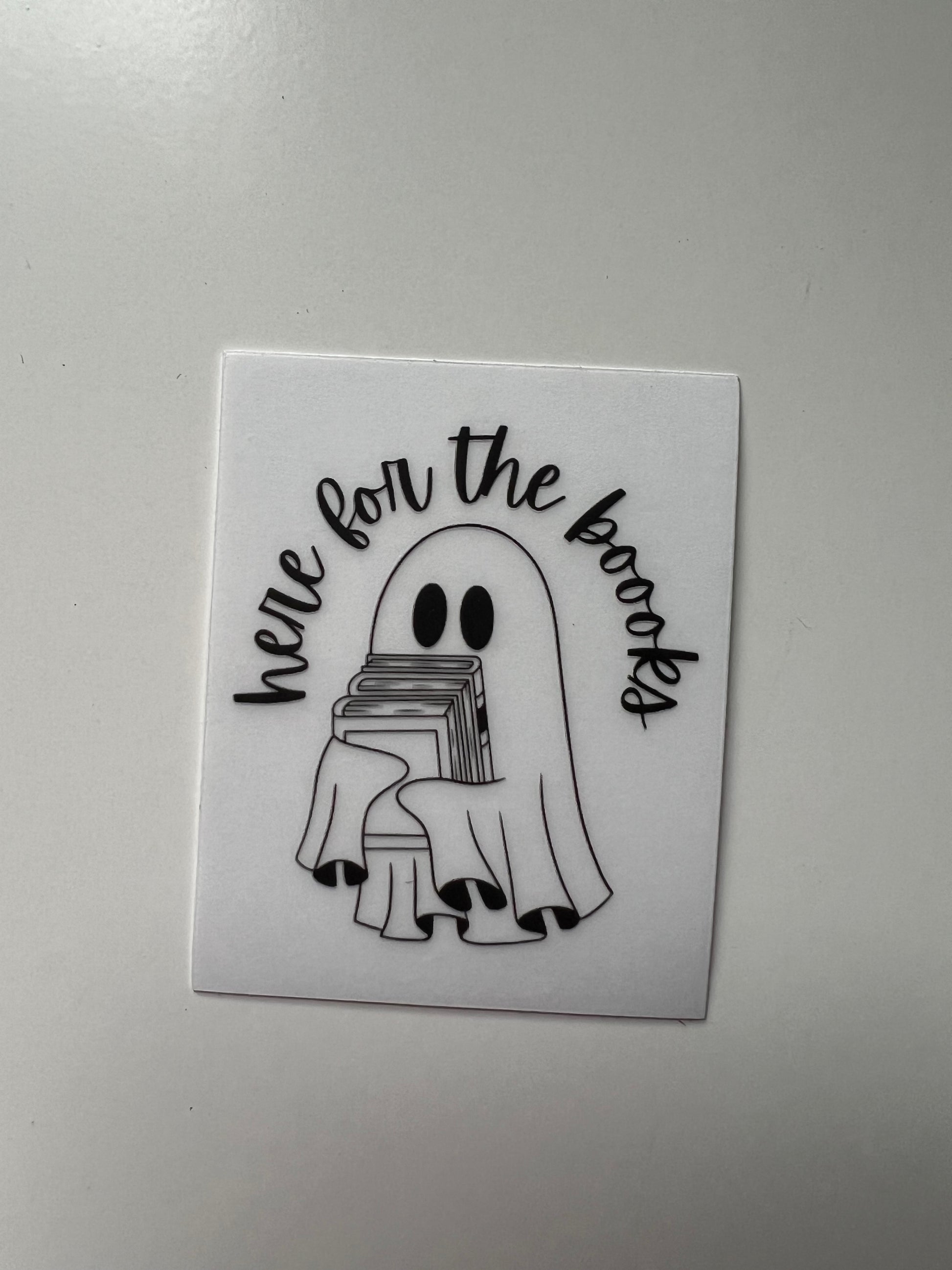 Clear vinyl sticker with a cute ghost holding a pile of books with curved text above it that says “here for the boooks”